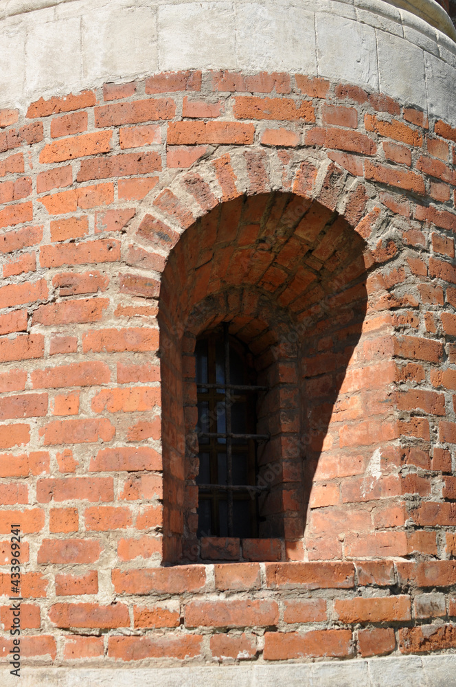 Small window in an old brick wall. Vaulted window with iron bars. The shade from the sun on the window.