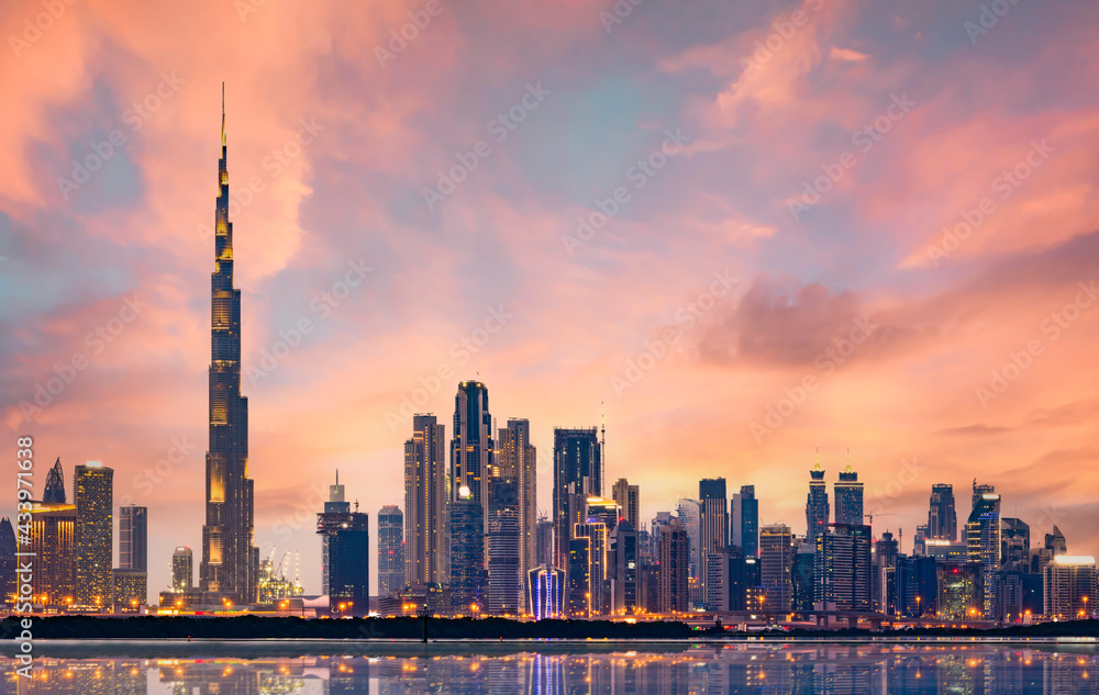 Stunning panoramic view of the illuminated Dubai skyline during a beautiful sunset. Silky smooth water flowing in the foreground. Dubai, United Arab Emirates.
