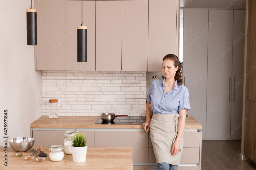 Portrait of young smiling female stands near table and baking on home kitchen interior background. Portrait of young smiling female stands near table and baking on home kitchen interior background.