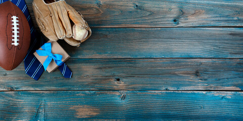 Football, baseball, mitt, necktie and giftbox on faded blue wood for happy fathers day concept
