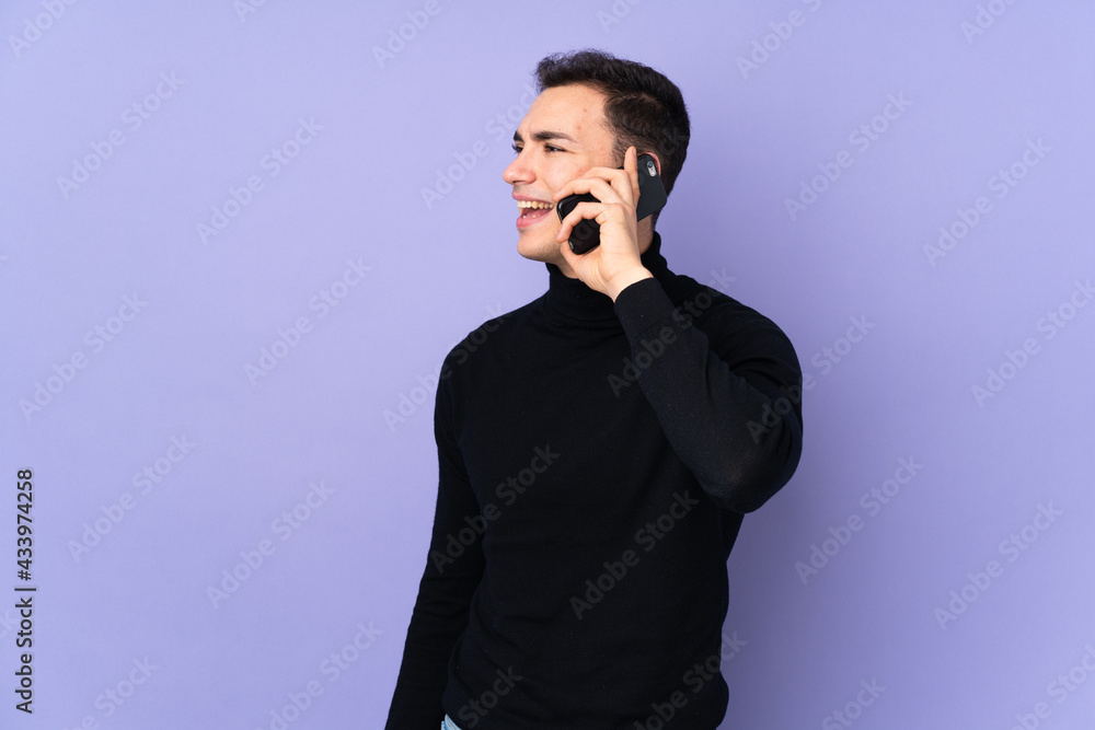 Young caucasian handsome man with turtleneck sweater isolated on purple background keeping a conversation with the mobile phone Young caucasian handsome man with turtleneck sweater isolated on purple background keeping a conversation with the mobile phone