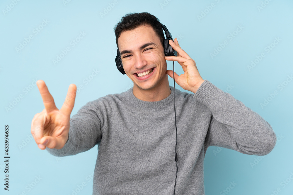 Fototapeta premium Young caucasian handsome man isolated on blue background listening music and singing