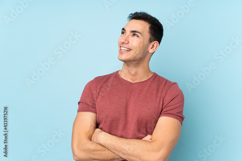 Young caucasian handsome man isolated on blue background looking up while smiling