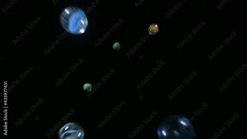 Marbles spheres fall into frame against black background in slow motion Marbles spheres fall into frame against black background in slow motion