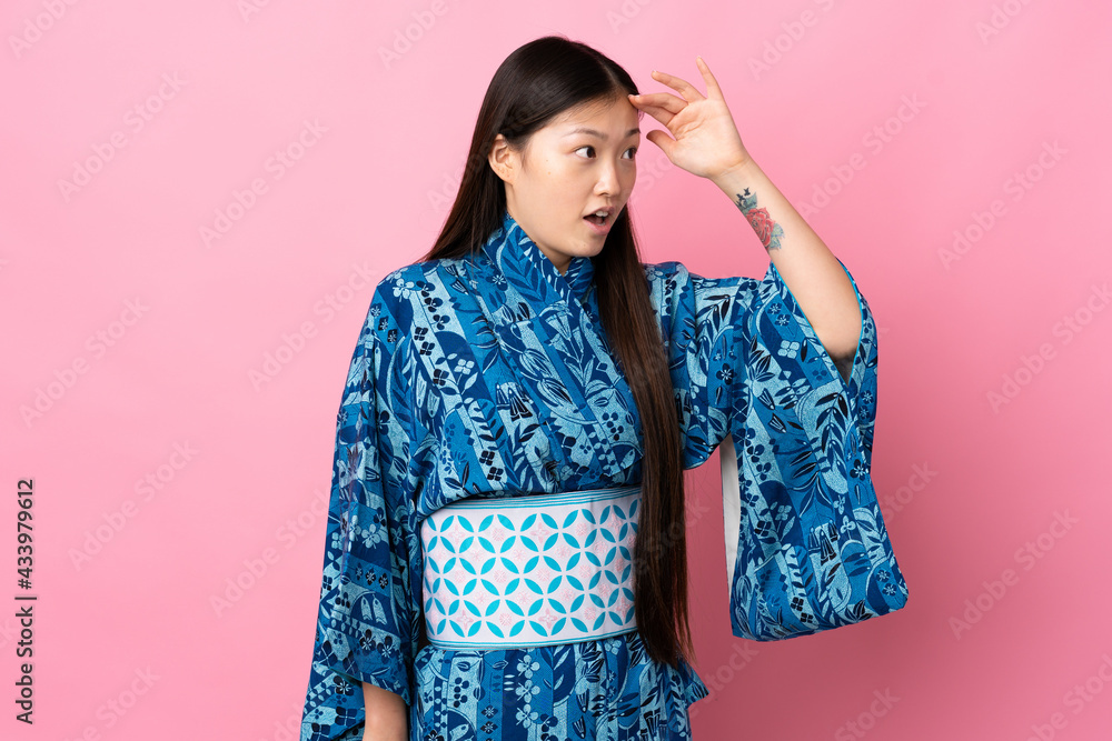Young Chinese girl wearing kimono over isolated background with surprise expression while looking side Young Chinese girl wearing kimono over isolated background with surprise expression while looking side
