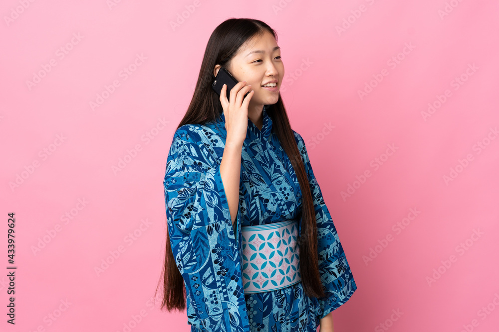 Young Chinese girl wearing kimono over isolated background keeping a conversation with the mobile phone
