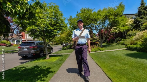 Postal worker hand delivering mail while walking down a sidewalk in a upscale neighborhood