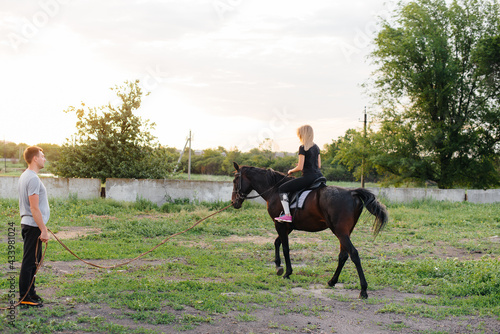 A young and pretty girl is learning to ride a thoroughbred Mare on a summer day at the ranch. Horse riding, training and rehabilitation © Andrii