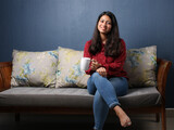 Young asian or indian girl drinking coffee on a sofa at home