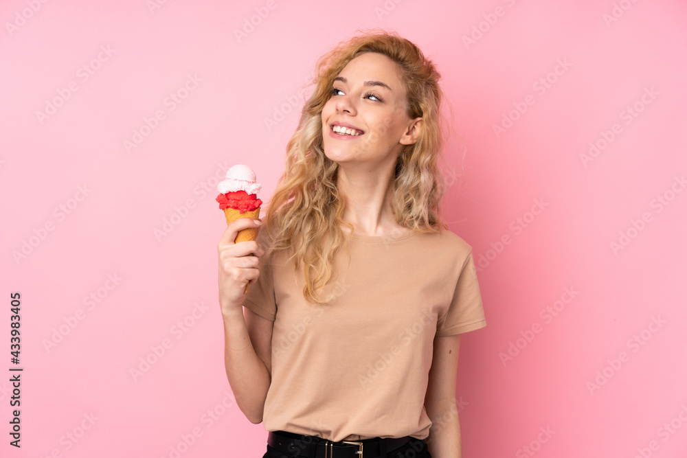 Young blonde woman holding a cornet ice cream isolated on pink background looking up while smiling Young blonde woman holding a cornet ice cream isolated on pink background looking up while smiling