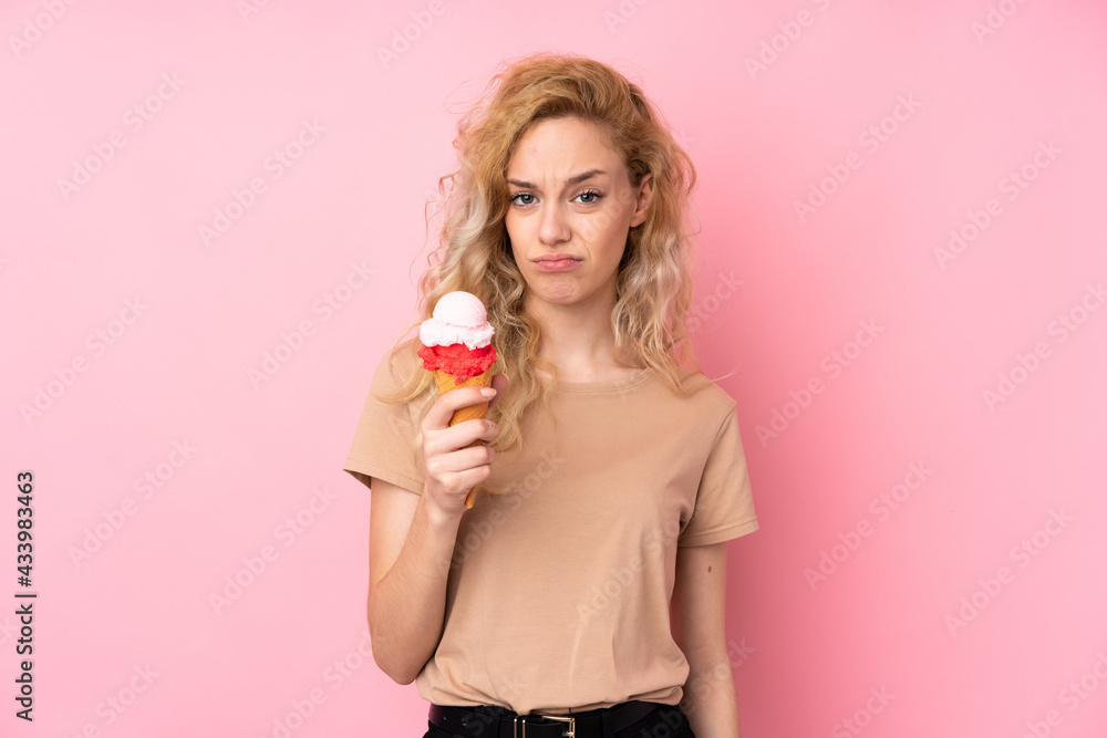 Young blonde woman holding a cornet ice cream isolated on pink background with sad expression Young blonde woman holding a cornet ice cream isolated on pink background with sad expression