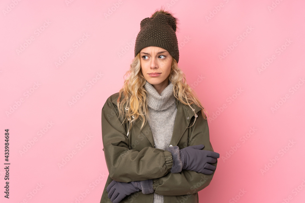 Young girl with winter hat isolated on pink background standing and looking to the side Young girl with winter hat isolated on pink background standing and looking to the side