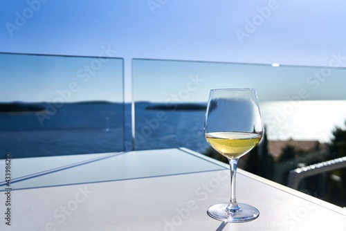 Glass of white wine on table on the terrace with the sea in the background. Summer vacation.