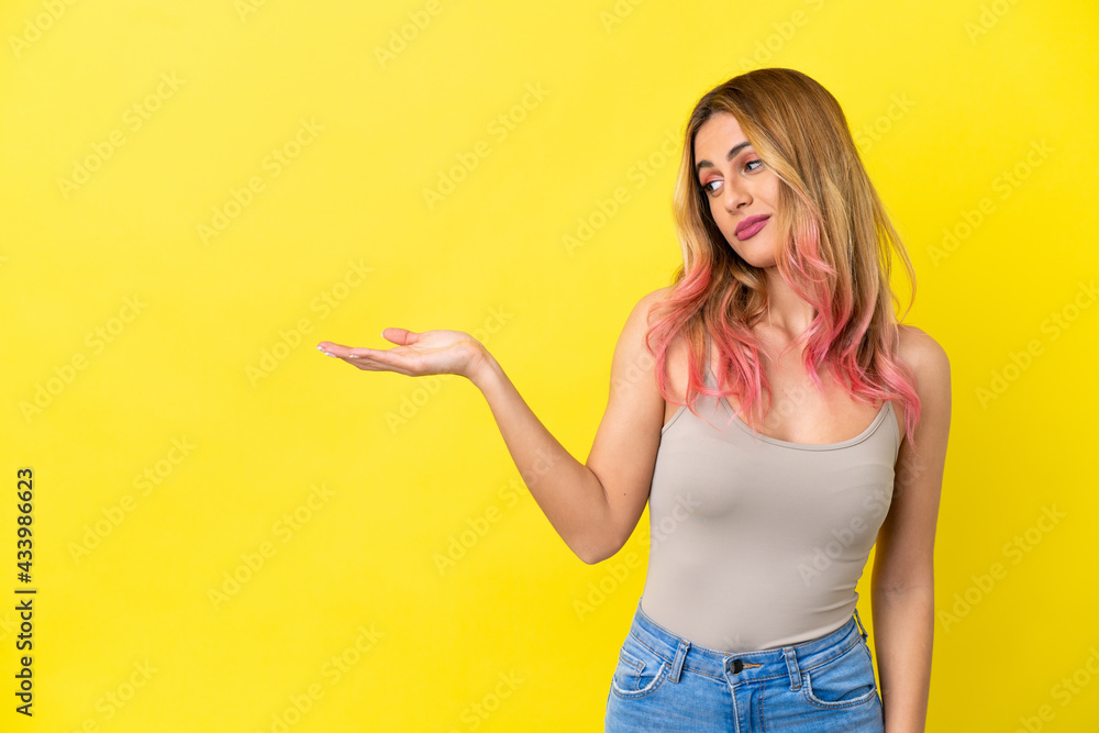 Young woman over isolated yellow background holding copyspace with doubts Young woman over isolated yellow background holding copyspace with doubts