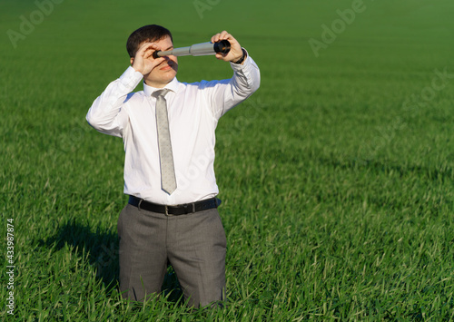 businessman poses with a spyglass, he looks into the distance and looks for something, green grass and blue sky as background