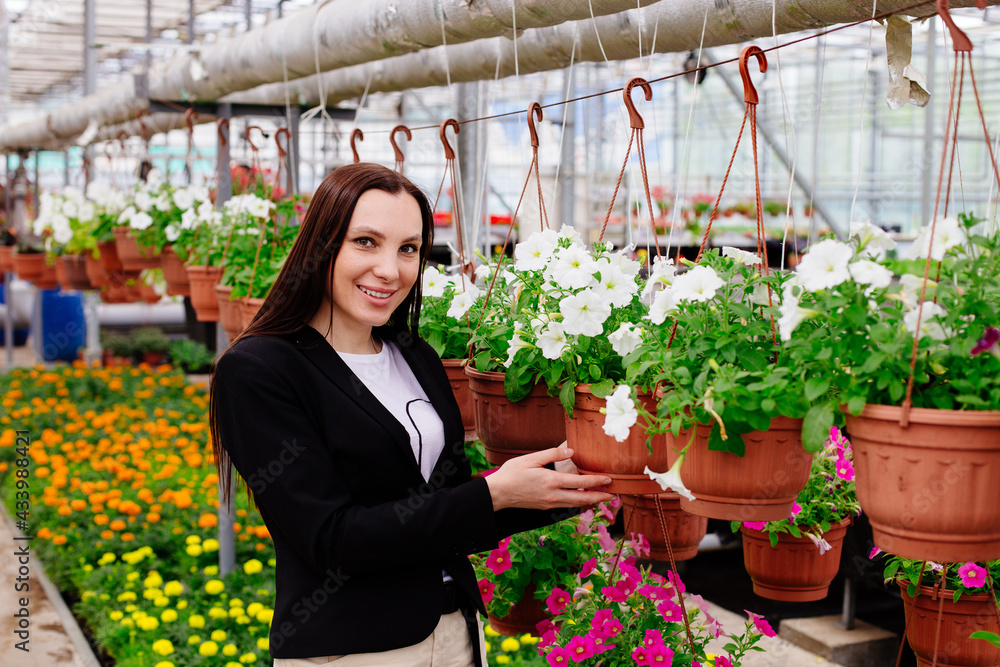 Attractive young woman with flowers in pot in greenhouse, gardening concept