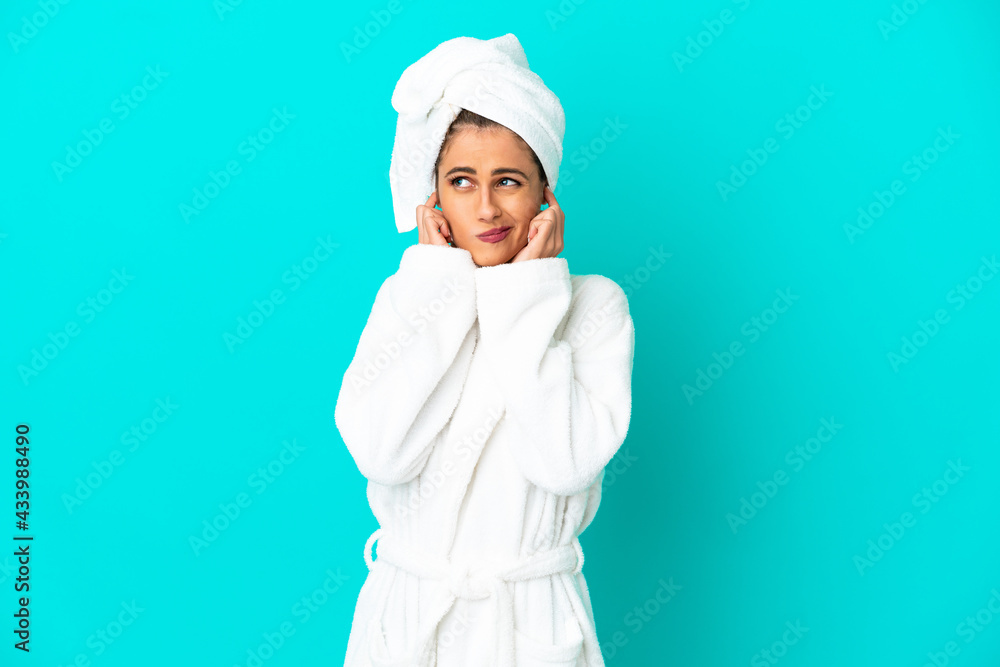 Young woman in a bathrobe over isolated blue background frustrated and covering ears Young woman in a bathrobe over isolated blue background frustrated and covering ears