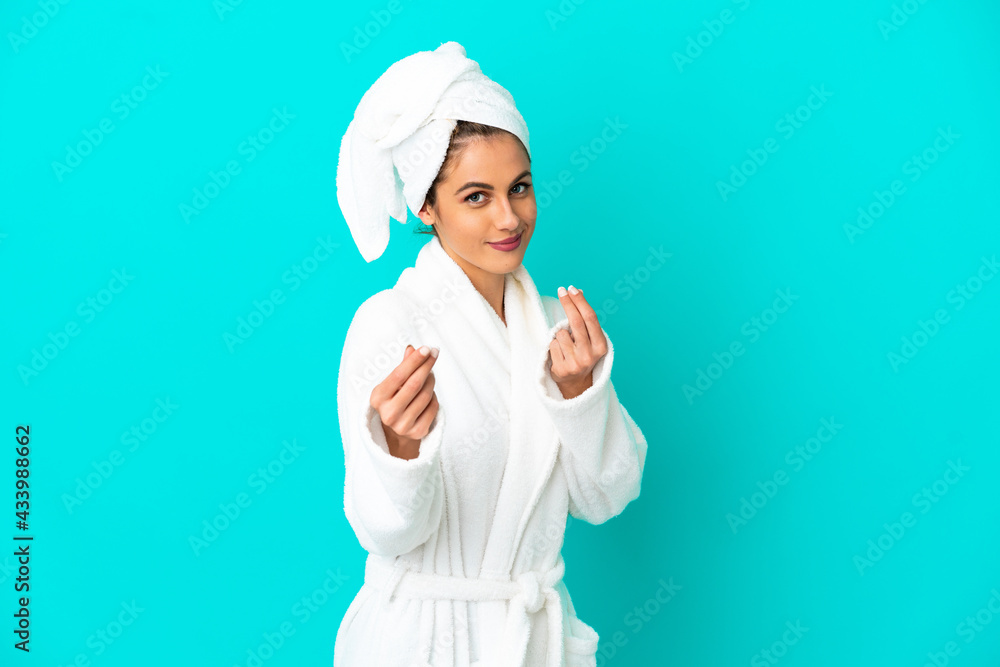 Young woman in a bathrobe over isolated blue background making money gesture Young woman in a bathrobe over isolated blue background making money gesture