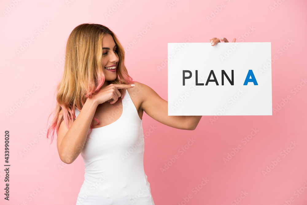 Young woman over isolated pink background holding a placard with the message PLAN A and pointing it Young woman over isolated pink background holding a placard with the message PLAN A and pointing it