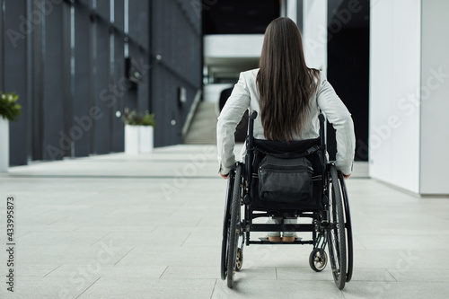 Back view full length at young businesswoman in wheelchair entering office building, copy space