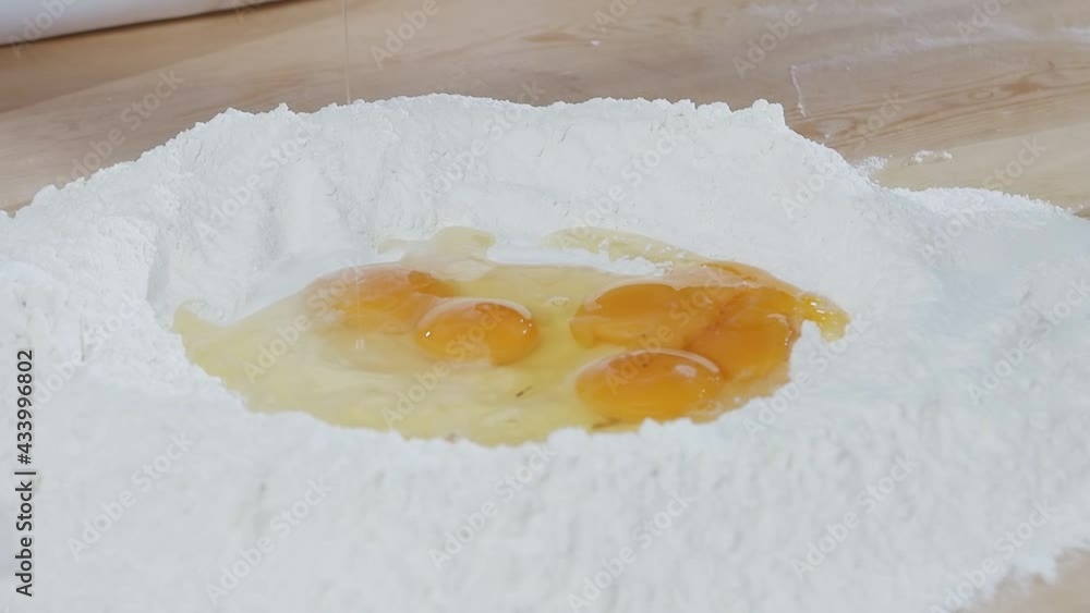Baker break eggs to the flour lying on the wooden cooking table. Slow motion Baker break eggs to the flour lying on the wooden cooking table. Slow motion