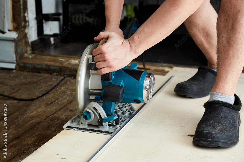 Sawing plywood by circular saw. Home repair. Hand tool. Man hold equipment. Building process. Woodworking. Safety engineering. Without gloves. Copy space. Indoor. Cutting material. Rental instrument Sawing plywood by circular saw. Home repair. Hand tool. Man hold equipment. Building process. Woodworking. Safety engineering. Without gloves. Copy space. Indoor. Cutting material. Rental instrument