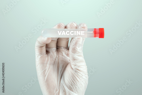 A gloved hand of a doctor holds a test tube with COVID-19 vaccine. Medical research, close-up.
