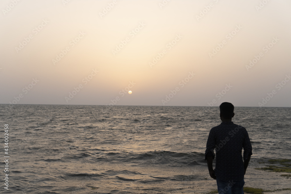 Silhouette of young man on the beach in ksa. Back view silhouette of a  man standing on the beach at sunset with sun in the.