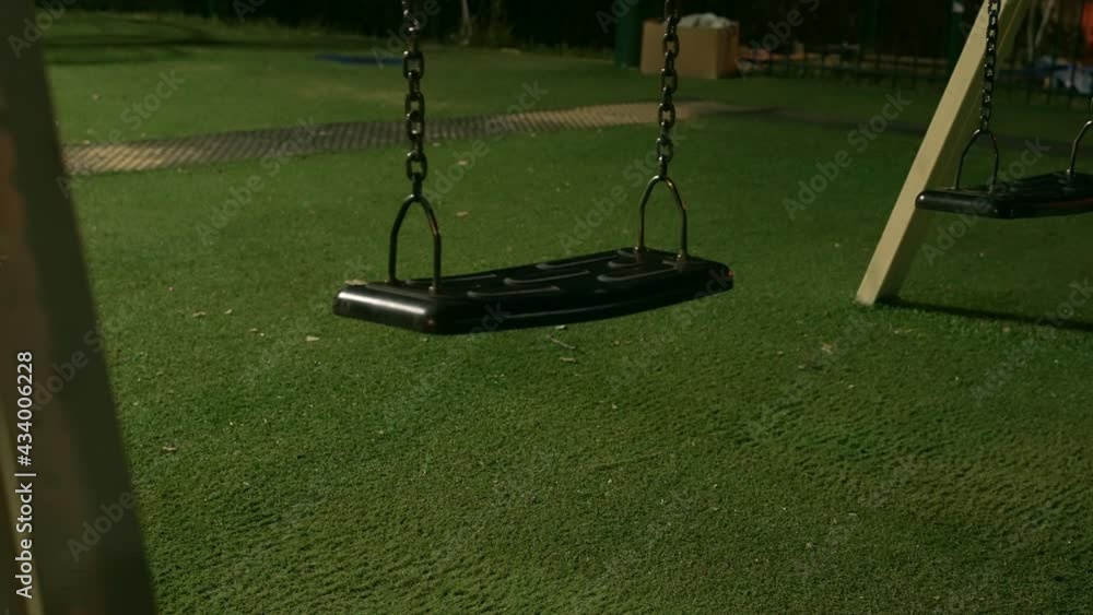 Empty swing in children's playground is swinging from side to side at
