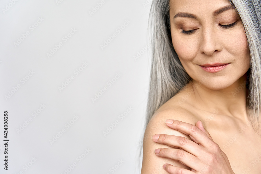 Fototapeta premium Mature older mid aged Asian woman of 50s with grey hair pampering her perfect skin. Advertising of body spa procedures for old women. Skincare, cosmetology, dermatology ads. Copy space.