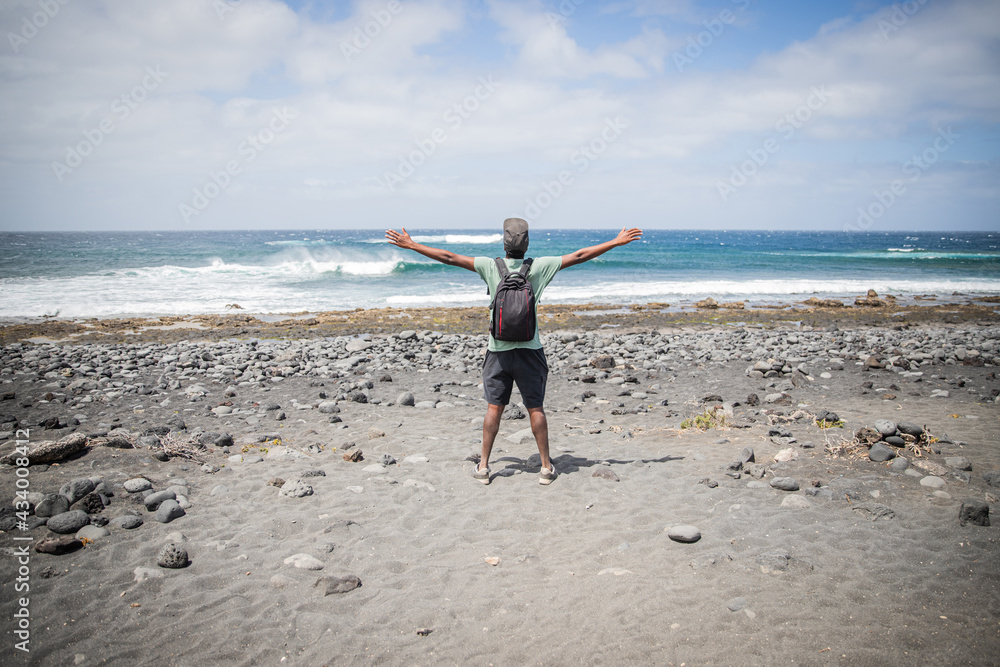 traveler boy at the beach opens his arms and looks at the sky, he is enjoying his trip and is happy. Traveler concept. traveler boy at the beach opens his arms and looks at the sky, he is enjoying his trip and is happy. Traveler concept.