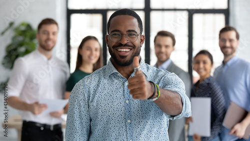 Portrait of happy African American male business leader making thumb up like gesture at camera. Employee satisfied with job and work with great team. Client giving positive feedback to company service photo
