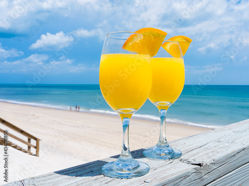 Glasses with an alcoholic cocktail mimosa with a slice of orange close up in the bright sun on the background of the beach