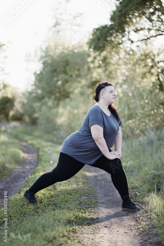 Puffy woman stretching legs at outdoor workout