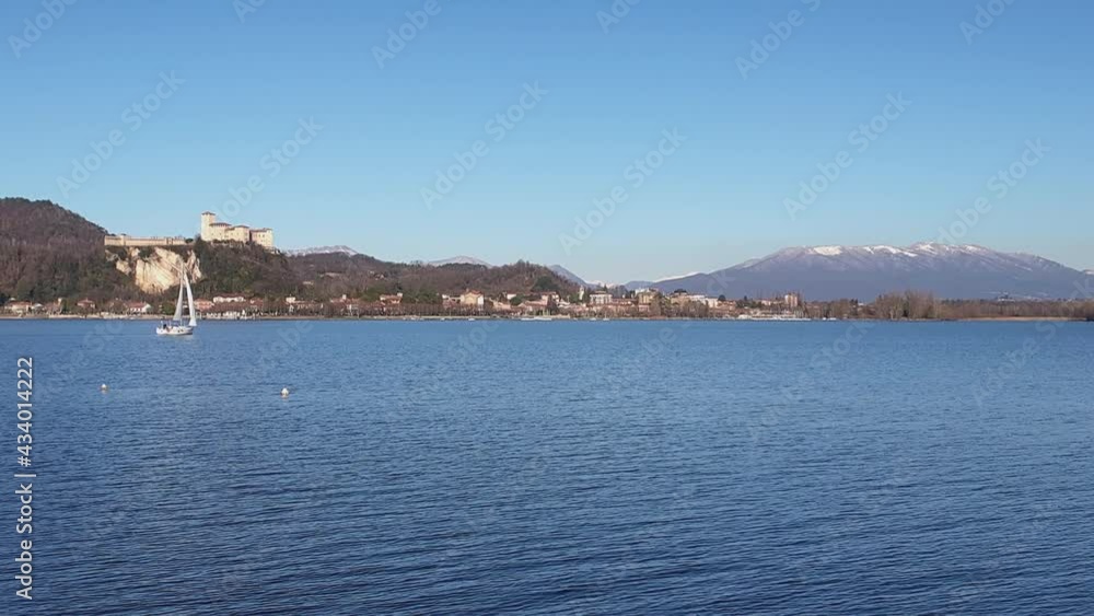 Small sailboat sailing on Maggiore lake in Piedmont with mountains and castle in background. Italy Small sailboat sailing on Maggiore lake in Piedmont with mountains and castle in background. Italy