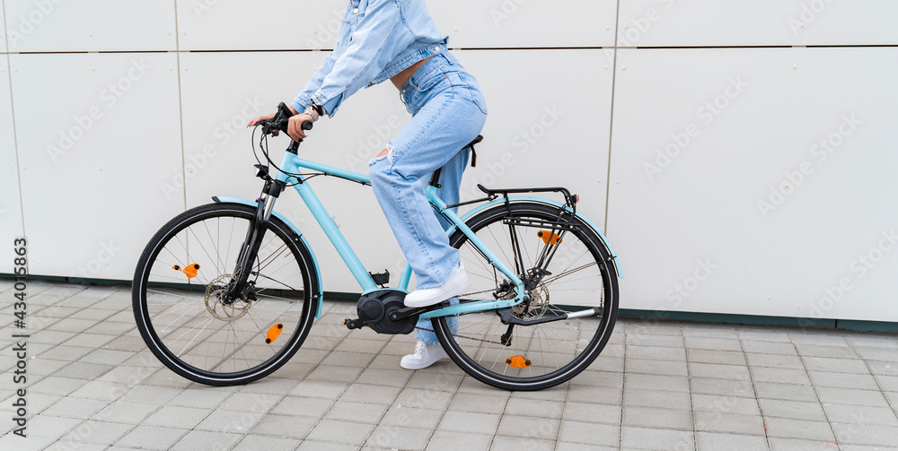 Naklejka premium Unrecognizable woman, no face shot, sitting on modern electric bicycle, white wall background 
