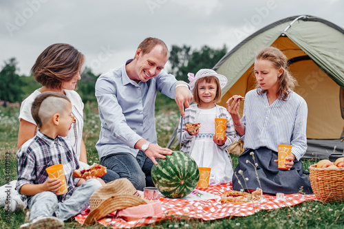 Happy family eating watermelon at picnic in meadow near the tent. Family Enjoying Camping Holiday In Countryside