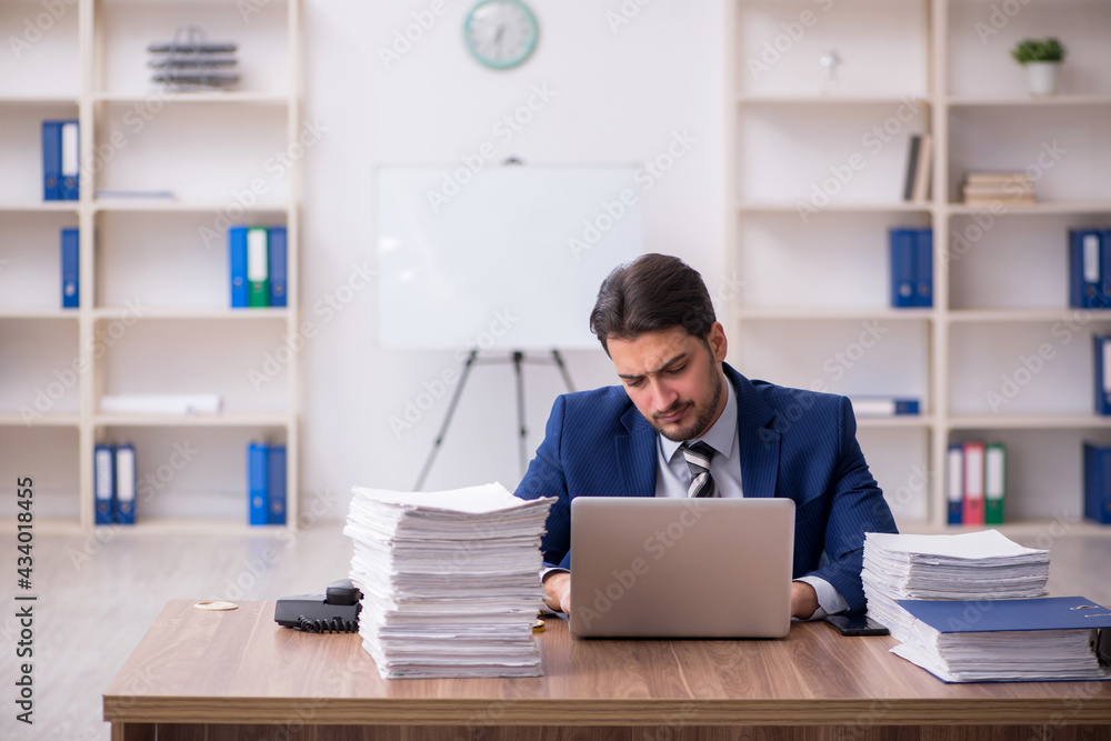 Young male employee unhappy with excessive work in the office Young male employee unhappy with excessive work in the office