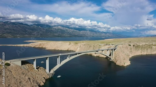 Paski Most - Boat Sailing Under Pag Bridge With Scenic Mountain View Under White Clouds In Croatia. - aerial photo