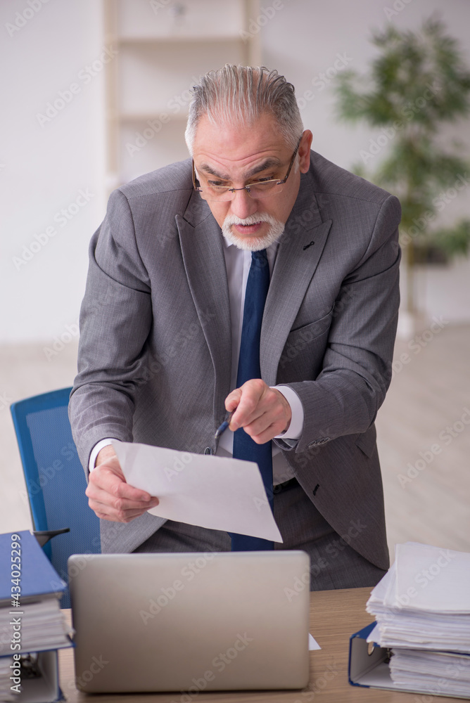 Old male employee unhappy with excessive work in the office Old male employee unhappy with excessive work in the office