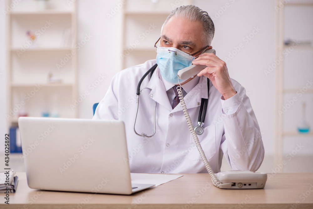 Old male doctor working in the clinic during pandemic Old male doctor working in the clinic during pandemic