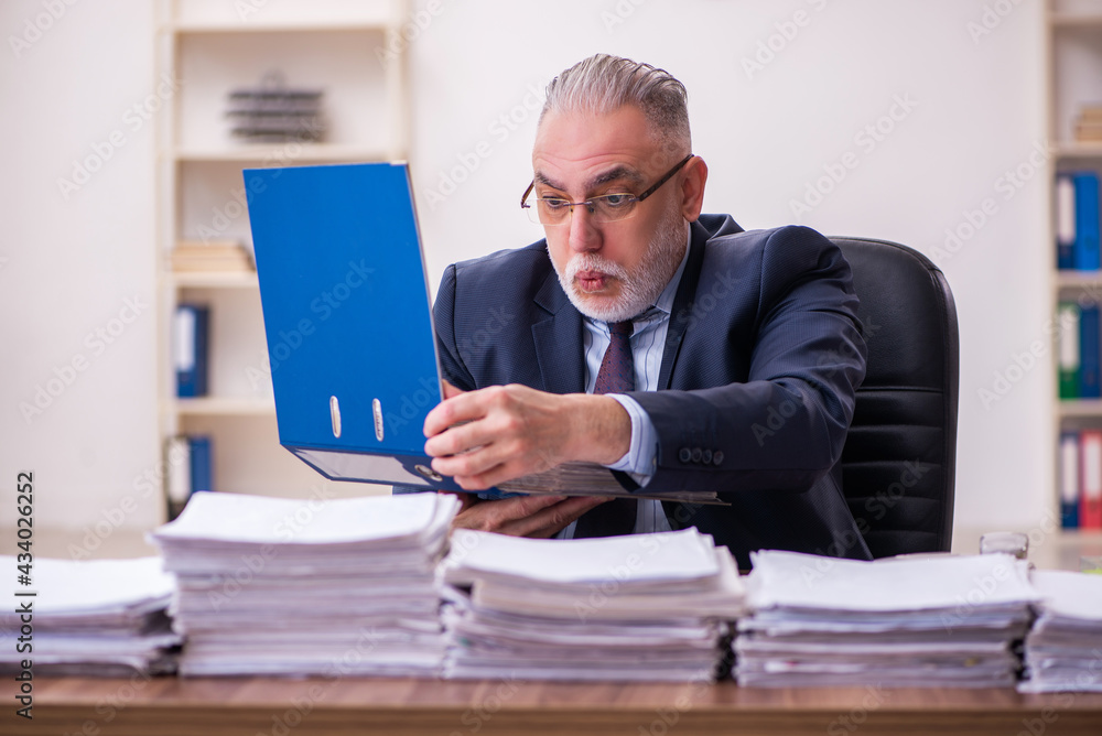 Old businessman employee unhappy with excessive work in the office Old businessman employee unhappy with excessive work in the office