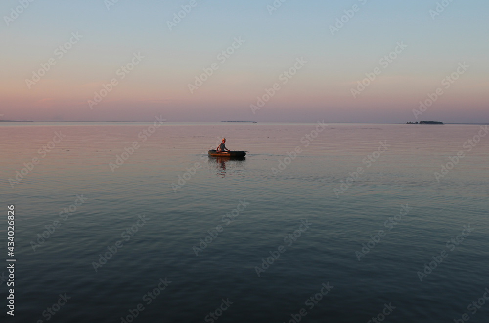 Russia, Novosibirsk 06.07.2019: male fisherman on a boat in the sea at sunset dawn on the waves
