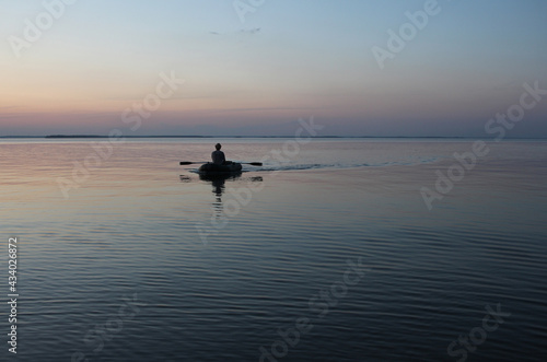 Russia, Novosibirsk 06.07.2019: male fisherman on a boat with oars sea at sunset dawn on the waves