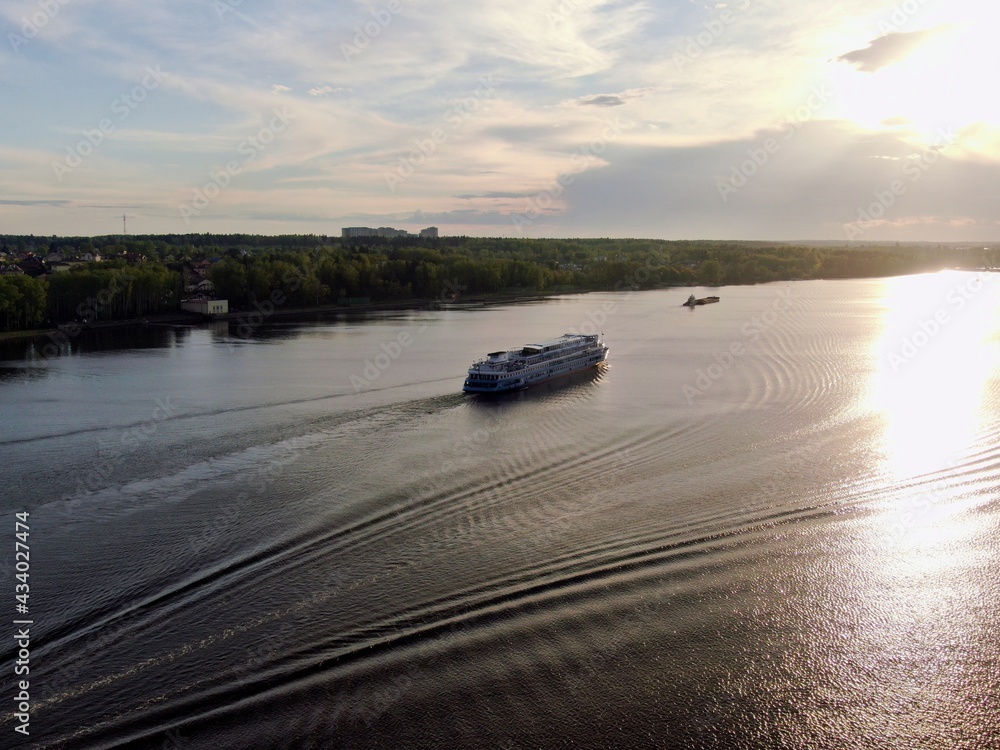 Aerial view passenger cruise ship sails along the river at sunset. Beautiful panorama of nature at sunset. Cruise trip. Aerial view passenger cruise ship sails along the river at sunset. Beautiful panorama of nature at sunset. Cruise trip.