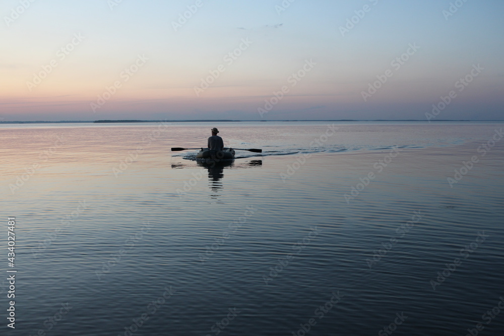 Russia, Novosibirsk 06.07.2019: male fisherman on a boat with oars sea at sunset dawn on the waves Russia, Novosibirsk 06.07.2019: male fisherman on a boat with oars sea at sunset dawn on the waves
