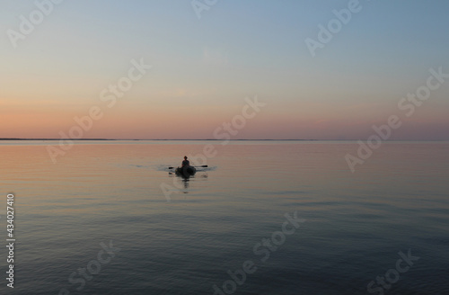 Russia, Novosibirsk 06.07.2019: male fisherman on a boat in the sea at sunset dawn on the waves