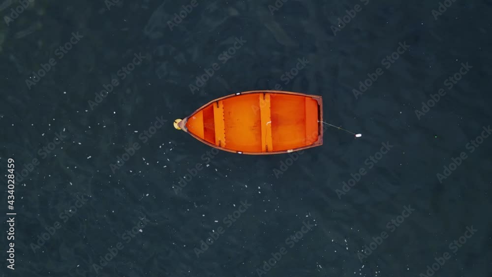 Drone shot flying upwards from a small red boat in the middle of the ocean with no one inside it Drone shot flying upwards from a small red boat in the middle of the ocean with no one inside it