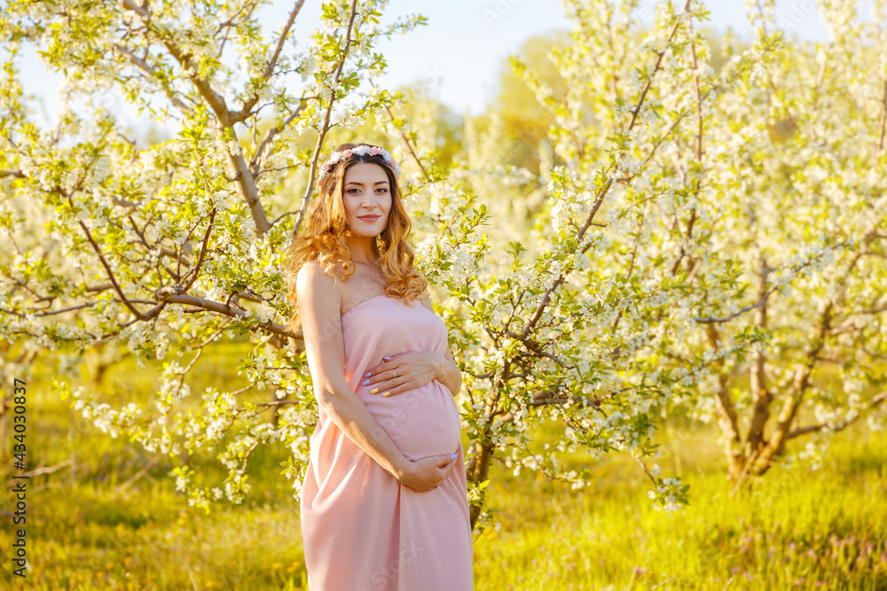 Pregnancy, motherhood, mothers day holiday concept. Happy pregnancy. Beautiful pregnant woman holds hands on belly in the spring garden. Young woman in maternity pink dress waiting for baby birth. Pregnancy, motherhood, mothers day holiday concept. Happy pregnancy. Beautiful pregnant woman holds hands on belly in the spring garden. Young woman in maternity pink dress waiting for baby birth.