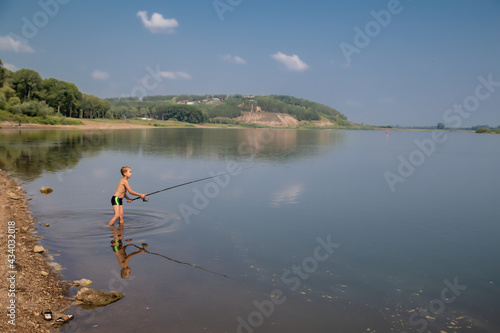 a little fisherman with a fishing rod on a hot summer day stands in the water